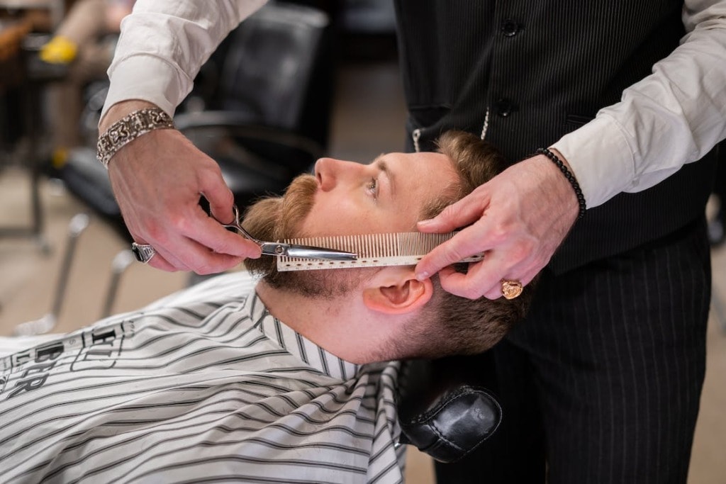 Barber cutting beard of his client.
